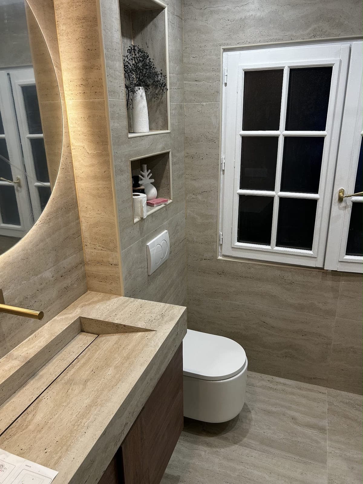 Salle de bain terminée en travertin : plan vasque taillé dans la masse, WC suspendu et miroir rétroéclairé