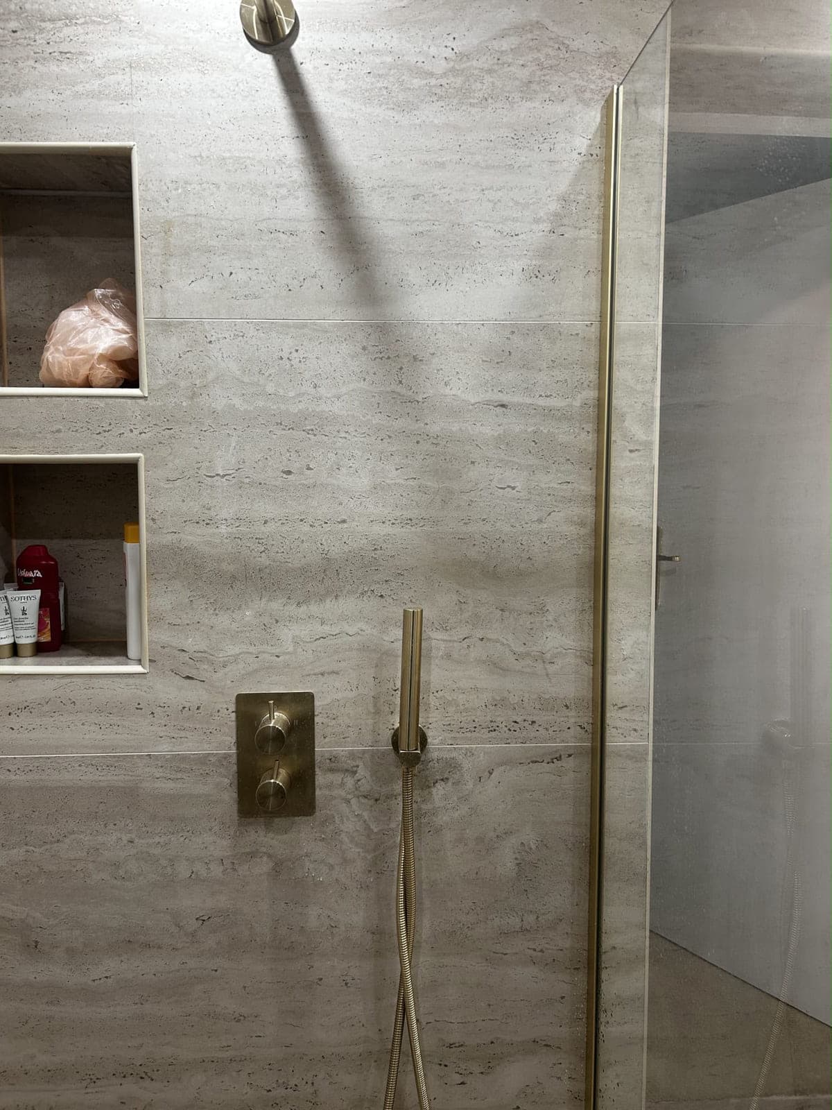 Douche en travertin avec niches de rangement et robinetterie encastrée dorée